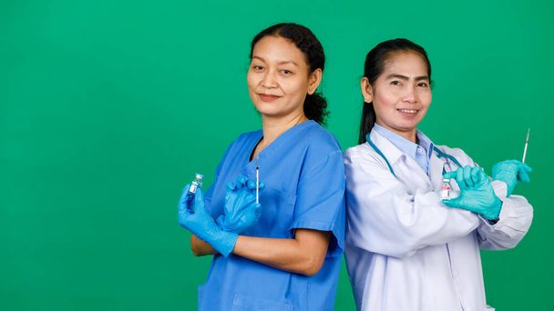 Azjatycka pielęgniarka w fartuchu i lekarz w białej todze trzymający strzykawkę i szczepionka Covid 19 przygotowująca do wstrzyknięcia. Koncepcja szczepienia szczepionką Covid 19. - Zdjęcie, obraz