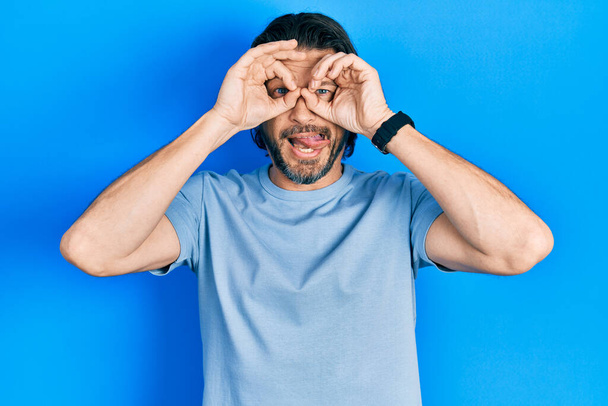 Middle age caucasian man wearing casual clothes doing ok gesture like binoculars sticking tongue out, eyes looking through fingers. crazy expression.  - Photo, image