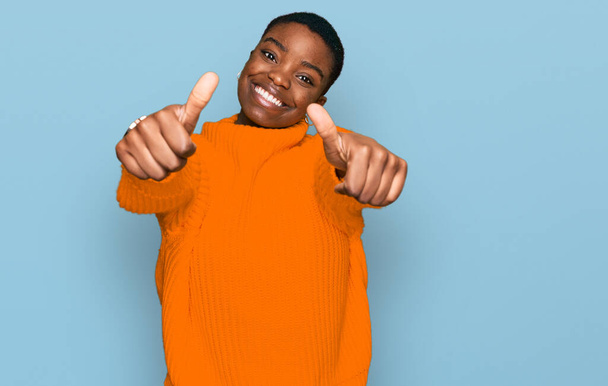 Jovem afro-americana vestindo roupas casuais aprovando fazer gesto positivo com a mão, polegar para cima sorrindo e feliz pelo sucesso. gesto vencedor.  - Foto, Imagem
