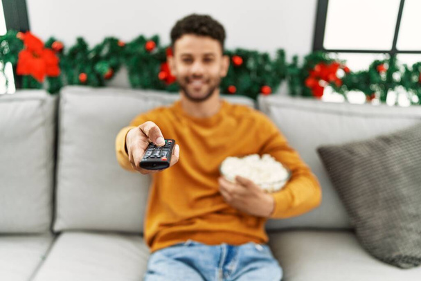 Young arab man watching movie sitting on the sofa by christmas decoration at home. - Fotografie, Obrázek