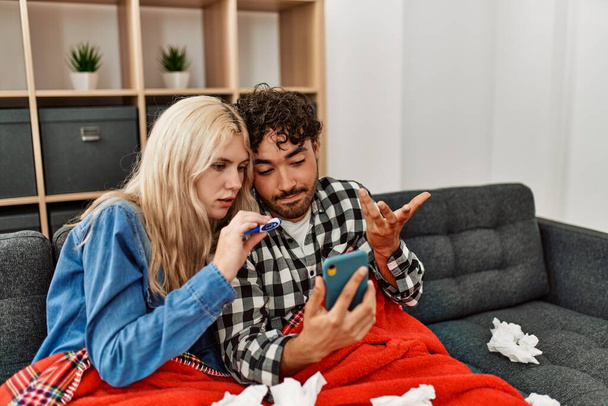 Young ill couple having medical teleconsultation using smartphone at home. - Foto, imagen