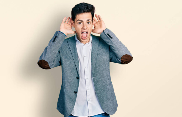 Young hispanic man wearing business clothes smiling cheerful playing peek a boo with hands showing face. surprised and exited  - Photo, Image