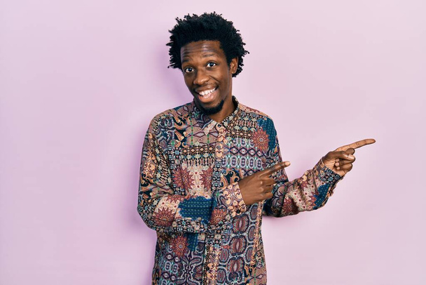Jeune homme afro-américain portant des vêtements décontractés souriant et regardant la caméra pointant avec deux mains et doigts sur le côté.  - Photo, image