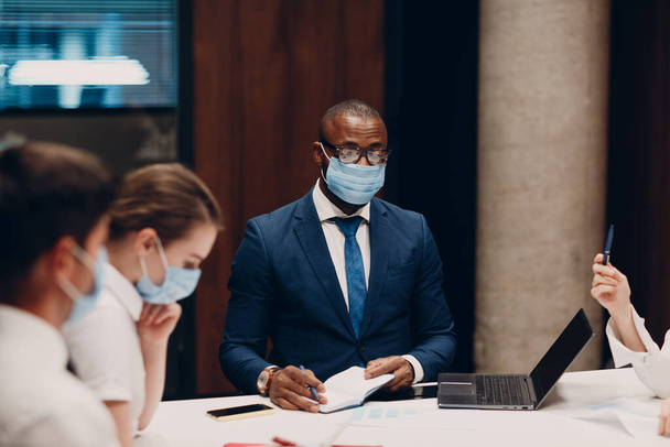 Συνάδελφοι διαφορετική ομάδα φορώντας μάσκα προσώπου συνάντηση γραφείο. Επιχειρηματίες άνδρες και γυναίκες ομάδα συζήτηση συνέδριο. - Φωτογραφία, εικόνα