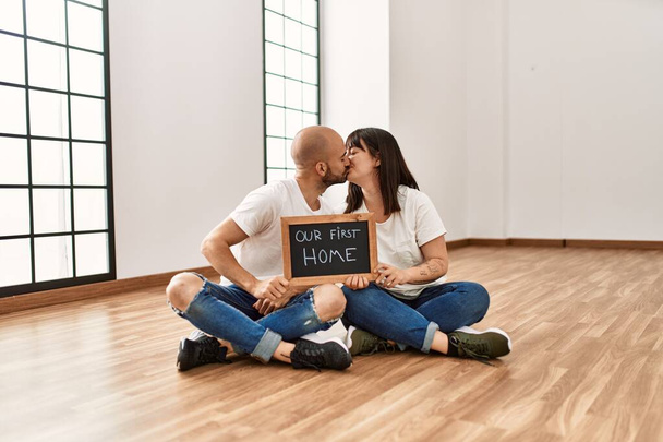 Young hispanic couple smiling happy holding our new home blackboard at empty new house. - Photo, Image