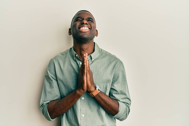 Jovem afro-americano vestindo roupas casuais implorando e orando com as mãos em conjunto com a expressão da esperança no rosto muito emocional e preocupado. implorando.  - Foto, Imagem