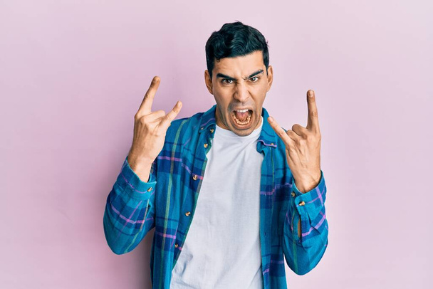 Handsome hispanic man wearing casual clothes shouting with crazy expression doing rock symbol with hands up. music star. heavy concept.  - Photo, Image