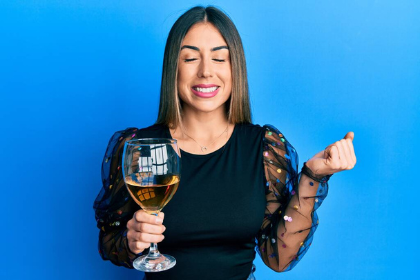 Young hispanic woman drinking a glass of red wine screaming proud, celebrating victory and success very excited with raised arm  - Photo, Image