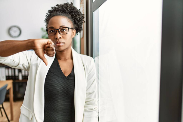 Afrykańska kobieta biznesu pracująca w biurze z wściekłą twarzą, negatywny znak pokazujący niechęć do kciuków w dół, koncepcja odrzucenia  - Zdjęcie, obraz