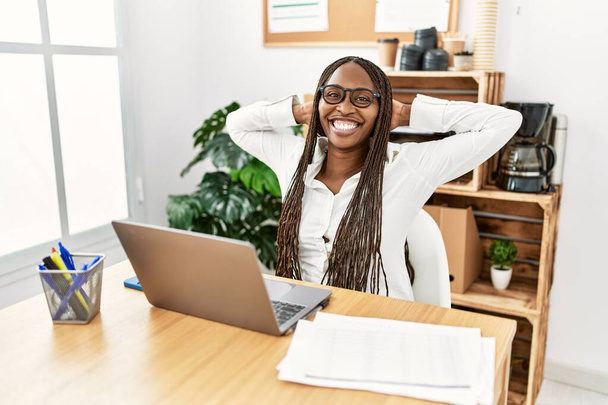 Νεαρή αφροαμερικανίδα επιχειρηματίας χαλαρή με τα χέρια στο κεφάλι στο γραφείο. - Φωτογραφία, εικόνα