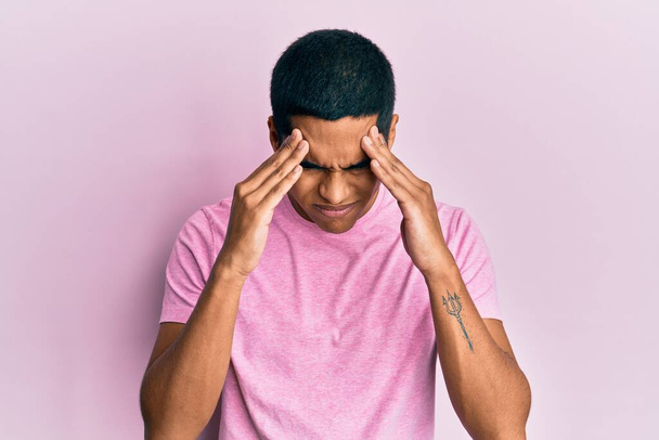 Молодий красивий іспаномовний чоловік в повсякденній рожевій сорочці з рукою на голову від болю в голові, тому що стрес. страждаюча мігрень
.  - Фото, зображення
