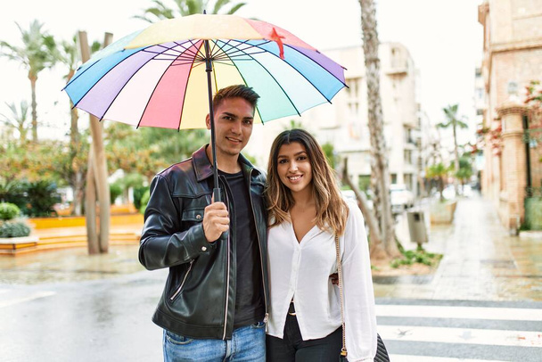 Jovem casal sorrindo feliz segurando guarda-chuva de pé na cidade. - Foto, Imagem