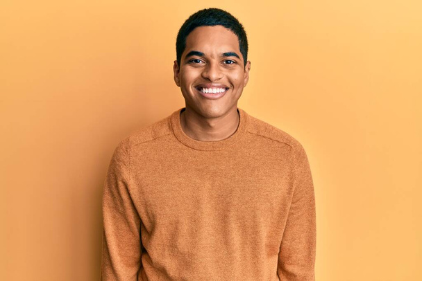 Νεαρός όμορφος Ισπανός που φοράει ένα απλό χειμωνιάτικο πουλόβερ με ένα χαρούμενο και δροσερό χαμόγελο στο πρόσωπο. τυχερό άτομο.  - Φωτογραφία, εικόνα