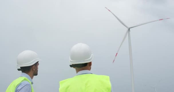 Engineers in white helmets look at operating wind turbine - Footage, Video