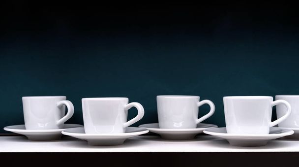 Witte koffiekopjes met schotels op een donkergroene achtergrond. - Foto, afbeelding