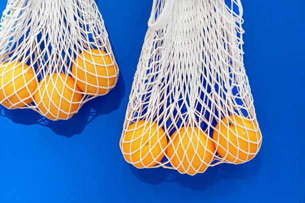 Соковиті апельсини в екологічно чистих сітчастих мішках на синьому фоні
. - Фото, зображення