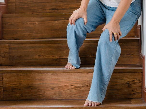 女性は足をかじりながら階段を登ることができない間、休息のために止まり、サポートのために壁にもたれています。ギラン・バリア症候群および麻痺脚疾患またはワクチン副作用の概念. - 写真・画像