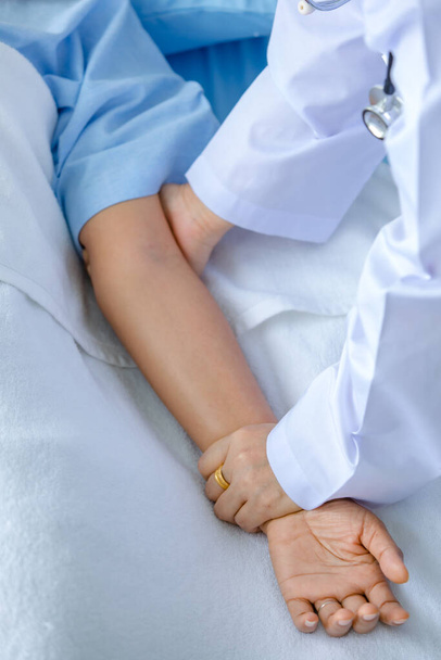 Dokter houdt hand van de patiënt op bed in het ziekenhuis en checkup zenuwstelsel voor genezing en behandeling. Concept van Guillain barre syndroom en gevoelloze handen ziekte of vaccin bijwerking. - Foto, afbeelding