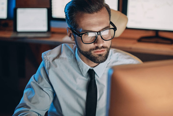 Serious young man working on computer while staying late in the office - 写真・画像