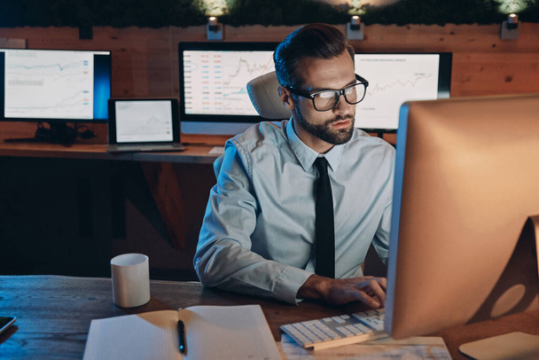 Концентрований молодий чоловік працює на комп'ютері, перебуваючи пізно в офісі
 - Фото, зображення