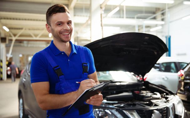 Confident and concentrated young and experienced car repair specialist with a tablet in his hand inspects and diagnosis the car for breakdowns - Фото, изображение