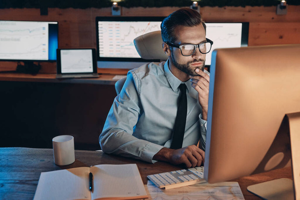 Концентрований молодий чоловік працює на комп'ютері, перебуваючи пізно в офісі
 - Фото, зображення
