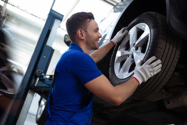 Handsome professional car mechanic changes a wheel on a car or carries out a tire change at a specialized auto repair center - 写真・画像