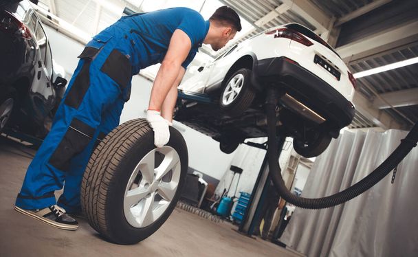 Handsome professional car mechanic changes a wheel on a car or carries out a tire change at a specialized auto repair center - Φωτογραφία, εικόνα
