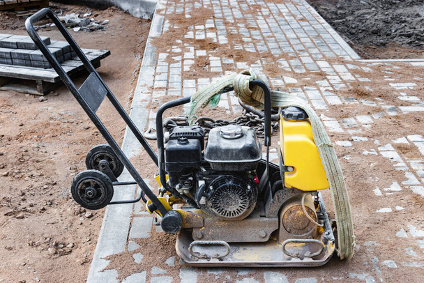 Vibratory rammer with vibrating plate on a construction site. Compaction of the soil before laying paving slabs. Close-up - Photo, Image
