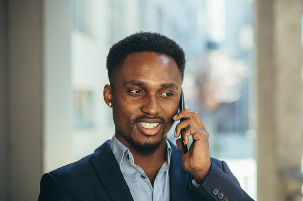close up portrait of african businessman talking on the phone and smiling from success in business suit - Foto, afbeelding