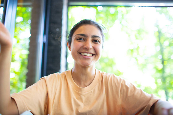 Снимок индийской женщины сидеть на Potdoor кафе размахивая рукой смотрит на камеру сделать видео-звонок чат с помощью компьютера веб-камера зрения, vlogger запись вебинара, собеседование удаленно концепция - Фото, изображение