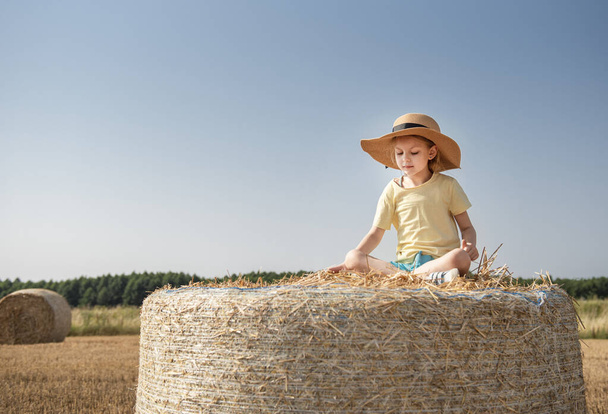 Niña divirtiéndose en un campo de trigo en un día de verano. Niño jugando en el campo de pacas de heno durante la cosecha. - Foto, Imagen
