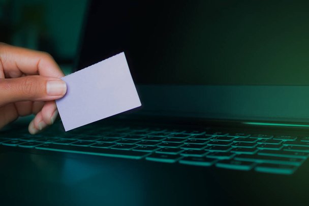 Ręczne trzymanie makiety pusty papier karty na laptopie klawiatury z zielonym na jasnym i czarnym ciemnym. haker, kradzież tożsamości, cyberbezpieczeństwo, cyfrowy internet technologii koncepcji online. - Zdjęcie, obraz