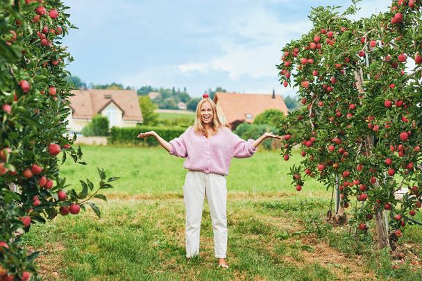Outdoor portrait of happy young woman in countryside, female model placed apple on her had, funny fashion lady - Photo, Image