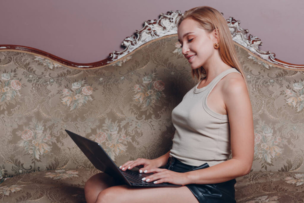 Young woman with blonde hair sitting and use laptop on couch - Photo, Image