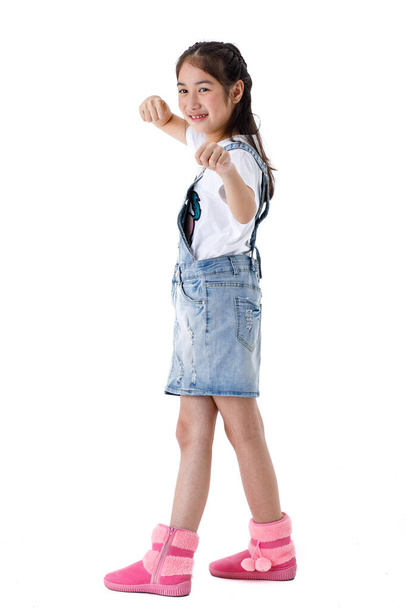 Портрет изолированной студии снимок молодых длинных волос довольно милая девушка в футболке и джинсовой юбке комбинезон с розовыми сапогами стоять и позировать с веселым действием на белом фоне. - Фото, изображение