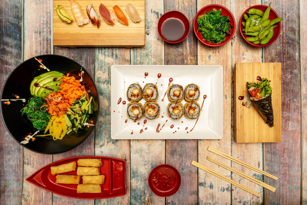 Top view image of sushi and asian food. Salmon poke bowl with wakame salad, edamame in pods, uramaki shrimp roll in tempura with nori seaweed. Smoked eel, shrimp and avocado nigiri - Photo, Image