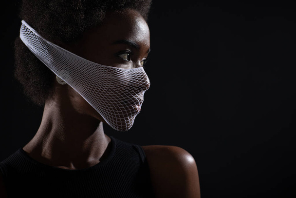 Closeup portrait of african american woman fashion model wearing quarantine medical face mask coarse mesh net on black background. Covid-19 coronavirus protection concept. - Photo, Image