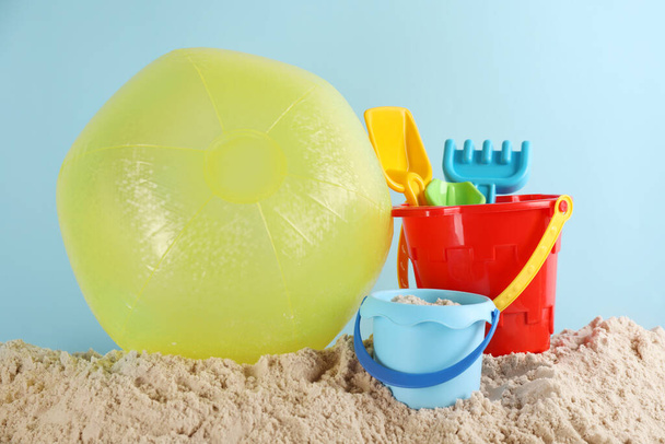Bright inflatable ball and plastic beach toys on sand against light blue background - Foto, afbeelding