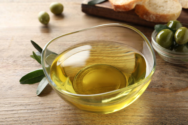 Glass bowl of olive oil on wooden table, closeup - Фото, изображение