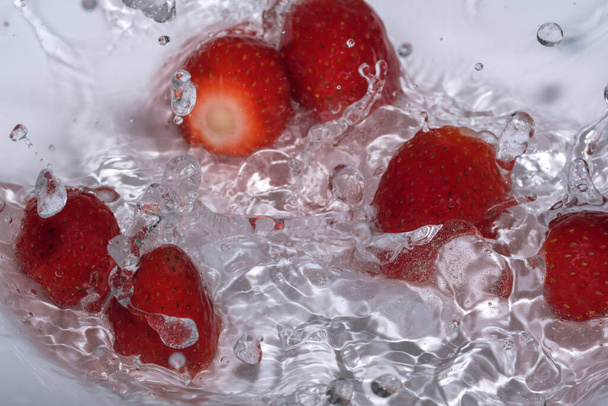 Ripe sweet fresh strawberry is washed in clean cold water with splashes and bubbles close-up - Фото, зображення