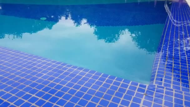 4k video, Superficie blu dell'acqua in una piscina all'aperto con piastrelle di mosaico blu. Il movimento dell'acqua increspature sullo sfondo di piastrelle di mosaico blu, il riflesso degli alberi - Filmati, video