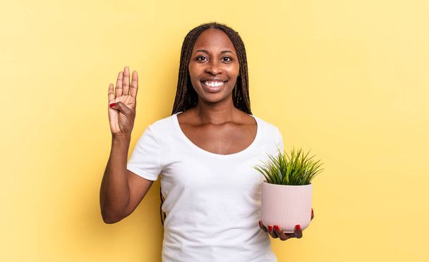 smiling and looking friendly, showing number four or fourth with hand forward, counting down holding a plant pot - Photo, Image