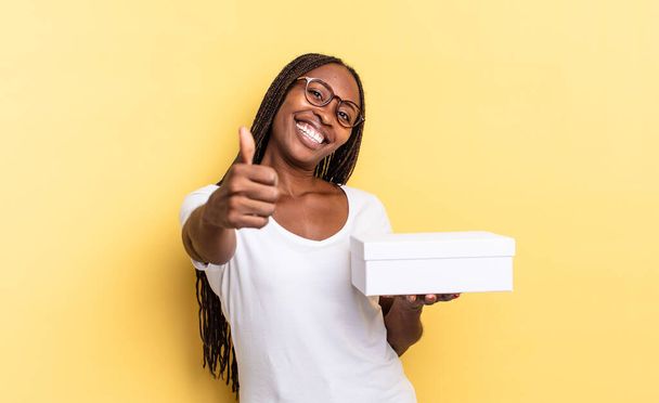 feeling proud, carefree, confident and happy, smiling positively with thumbs up and holding an empty box - Fotoğraf, Görsel