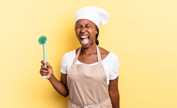 black afro chef woman shouting aggressively, looking very angry, frustrated, outraged or annoyed, screaming no. cleaning dishes concept - Fotografie, Obrázek
