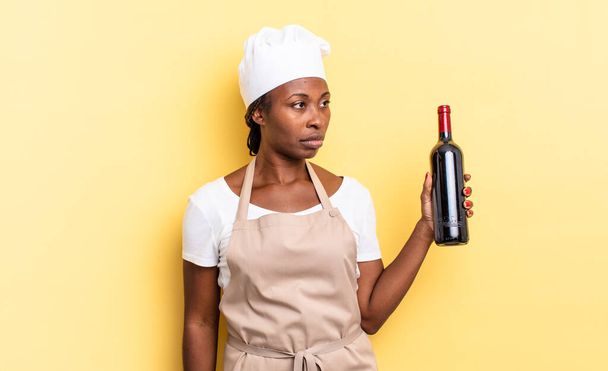 black afro chef woman feeling sad, upset or angry and looking to the side with a negative attitude, frowning in disagreement. wine bottle concept - Photo, Image