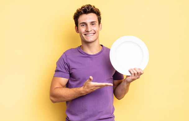 smiling cheerfully, feeling happy and showing a concept in copy space with palm of hand. empty plate concept - Photo, image