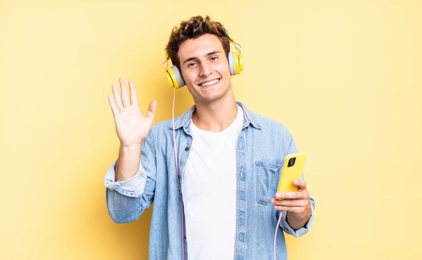 smiling happily and cheerfully, waving hand, welcoming and greeting you, or saying goodbye. headphones and smartphone concept - 写真・画像