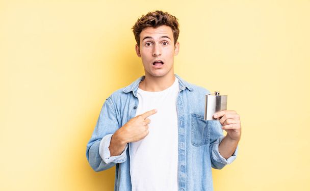 looking shocked and surprised with mouth wide open, pointing to self. alcohol flask concept - Foto, imagen