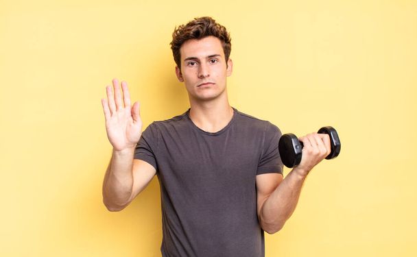 looking serious, stern, displeased and angry showing open palm making stop gesture. dumbbell concept - Фото, изображение